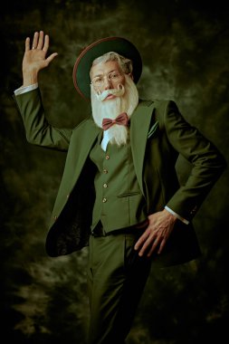 Moda ve tarz. Zarif beyaz sakallı ve bıyıklı üç parçalı takım elbiseli iyi giyimli bir Noel Baba klasik bir arka planda poz verir. Noel ve Yeni Yıl.