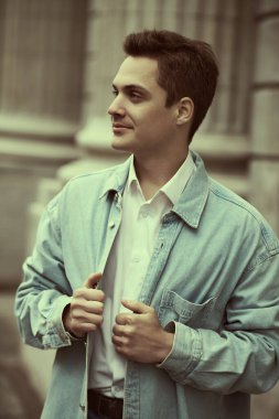 Bulutlu bir günde, kot gömlekli yakışıklı, modern bir adam şehir caddesinde duruyor. İnsanlar ve duygular, yaşam tarzı.