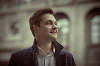 İnsanlar ve duygular. Paltolu yakışıklı, modern bir adam bulutlu bir günde bir şehir caddesinde duruyor ve gülümsüyor. Yaşam biçimi.