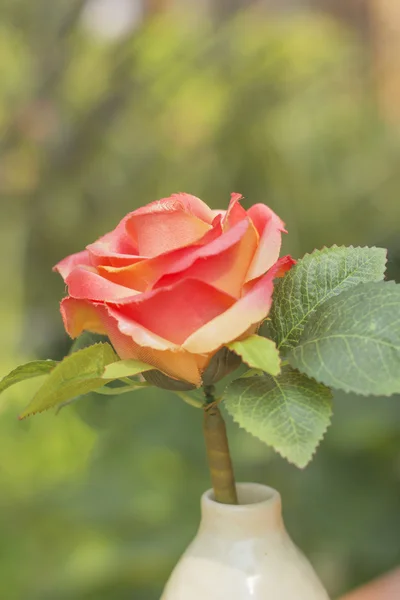 Rosas artificiales en un jarrón blanco contra la naturaleza borrosa backgroun — Foto de Stock