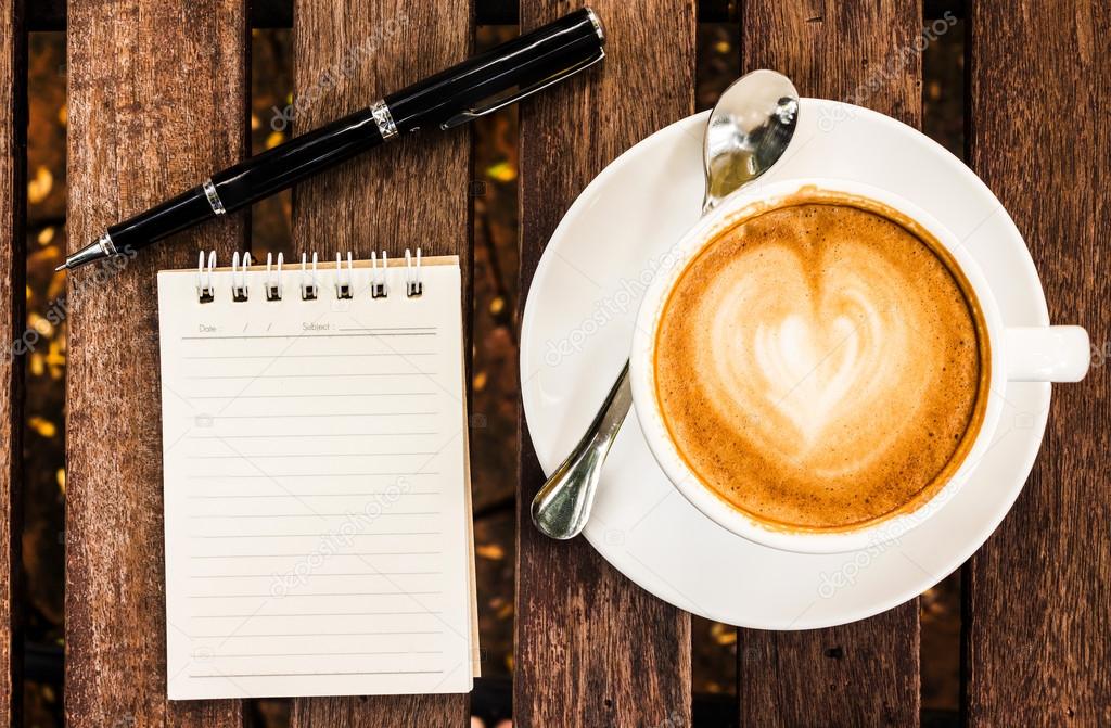 Open a blank white notebook, pen and cup of coffee on wood desk 