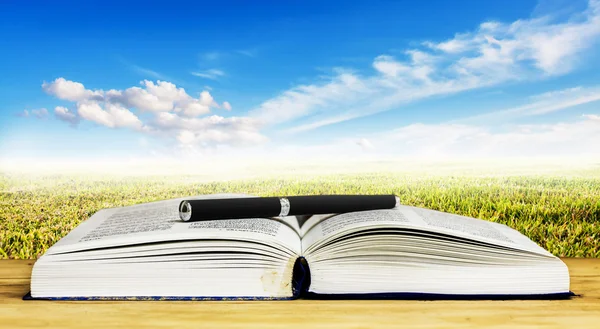 Libro abierto y pluma sobre mesa de madera contra cielo azul con nube — Foto de Stock