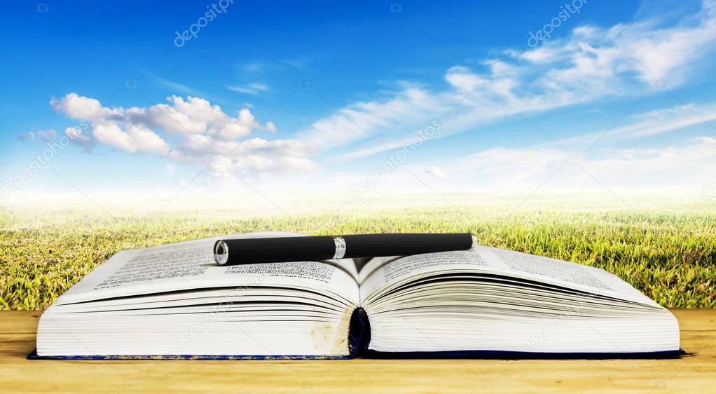 Open book and pen on wood table against blue sky with cloud