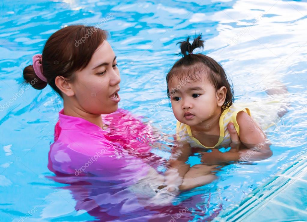 Asian young mother is teaching little daughter to swim happily i