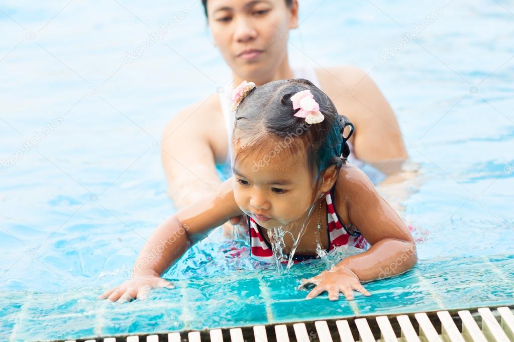 Young mother teaching cute baby girl how to swim in a swimming p