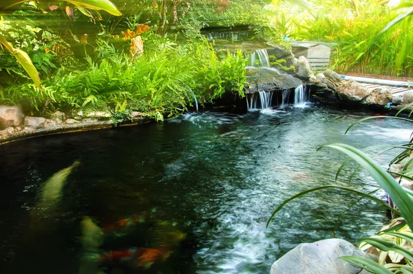 Waterfall in garden design with artificial sunlay. — Stock Photo, Image