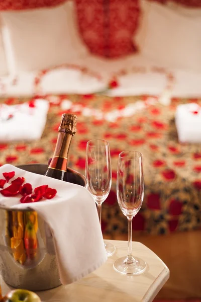 Sparking wine, champagne glasses and rose petals on a table in a romantic spa hotel room. Royalty Free Stock Photos