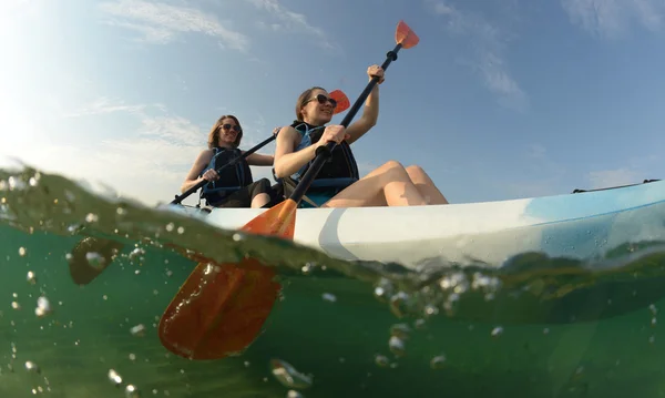 Dos mujeres jóvenes remando kayak azul Fotos De Stock Sin Royalties Gratis