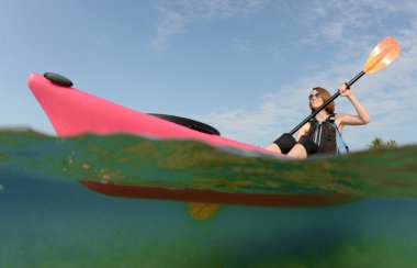 Genç ve güzel kadın tropikal okyanusta bir kayık kürek çekmeye