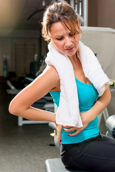 Chica en el gimnasio sosteniendo una mano de una espalda enferma — Foto de Stock