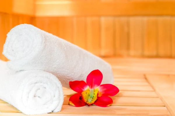 Asciugamani di spugna ritorti e un fiore tropicale nella sauna — Foto Stock