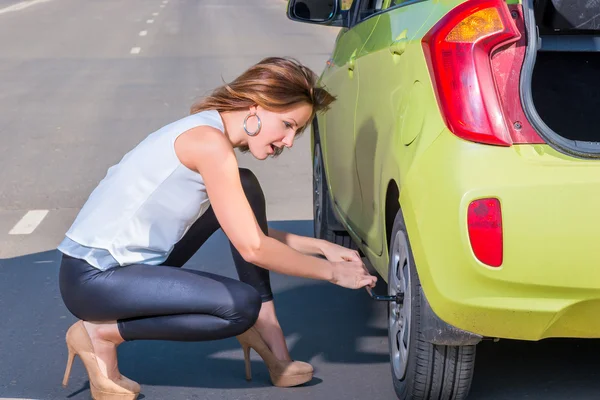 Slender beautiful woman unscrews spanner car wheel — Stock Photo, Image