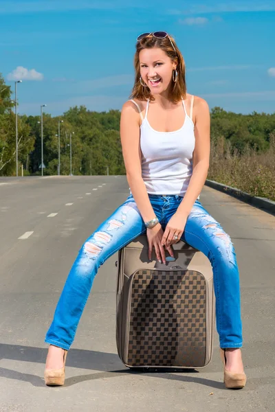 Happy girl with a suitcase on the road on a sunny day — Stock Photo, Image