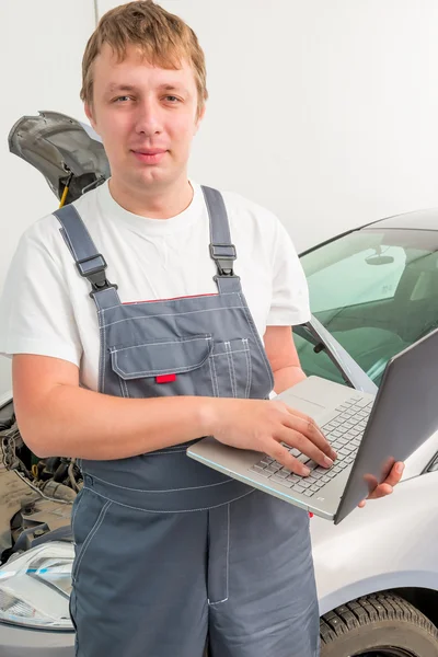 Ingenjör i mekanik med en laptop nära en bil i ett garage — Stockfoto