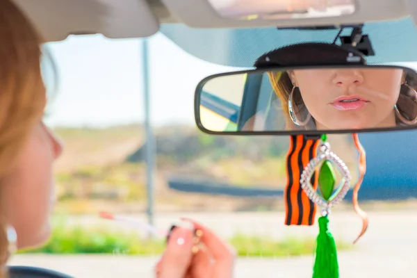 Girl applies lipstick behind the wheel of the car while driving — Stock Photo, Image