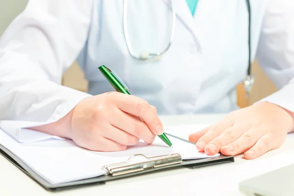 Dokter in een witte jas schrijft op een recept van papier — Stockfoto