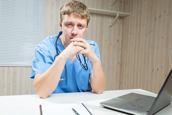 Cansado médico sostiene en manos gafas sentado a la mesa — Foto de Stock