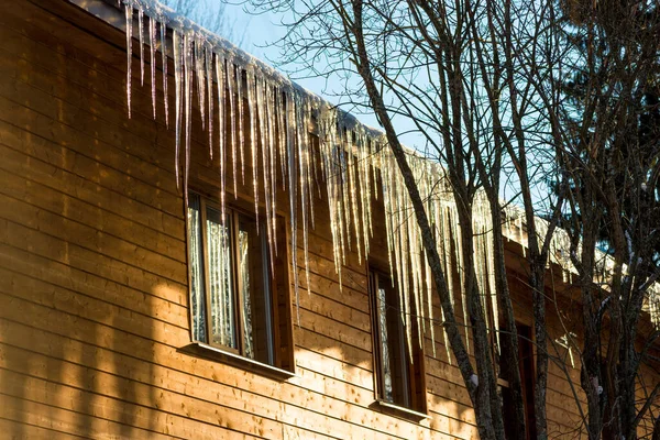 大きなつららが家の屋根から吊るされている 家の中の危険な大きなつらら — ストック写真