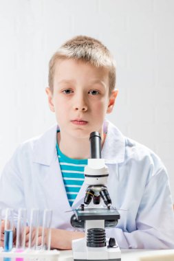 Mikroskobu olan bir öğrenci test tüplerindeki kimyasalları inceliyor, deneyler yapıyor - beyaz arka planda bir portre. Laboratuvarda koronavirüs incelemesi konsepti