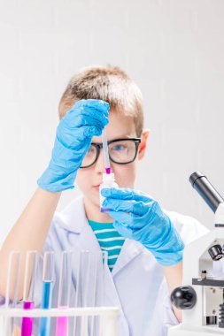 Mikroskobu olan bir öğrenci test tüplerindeki kimyasalları inceliyor, deneyler yapıyor - beyaz arka planda bir portre. Laboratuvarda koronavirüs incelemesi konsepti