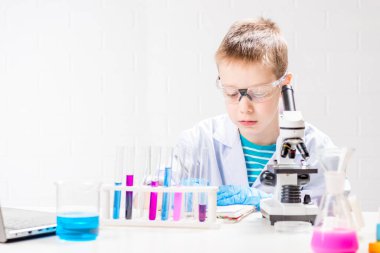 Mikroskobu olan bir öğrenci test tüplerindeki kimyasalları inceliyor, deneyler yapıyor - beyaz arka planda bir portre. Laboratuvarda koronavirüs incelemesi konsepti