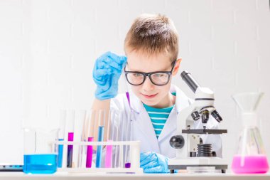 Mikroskobu olan bir öğrenci test tüplerindeki kimyasalları inceliyor, deneyler yapıyor - beyaz arka planda bir portre. Laboratuvarda koronavirüs incelemesi konsepti