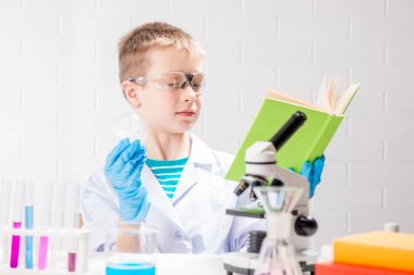 Elinde mikroskop ve kitap olan bir öğrenci test tüplerindeki kimyasalları inceliyor, deneyler yapıyor - beyaz arka planda bir portre. Laboratuvarda koronavirüs incelemesi konsepti