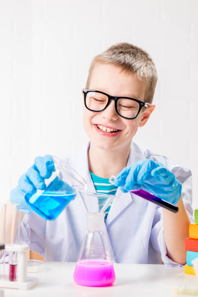 A schoolboy studies multi-colored substances in test tubes, conducts experiments - a portrait on a white background. Concept for the study of coronavirus in the laboratory