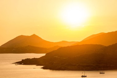Turuncu gökyüzü ve siluet dağ arkaplanlı günbatımı deniz manzarası