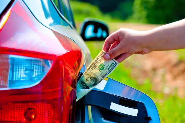 Kvinnlig hand sätter bilen i bensintanken hundra dollar — Stockfoto