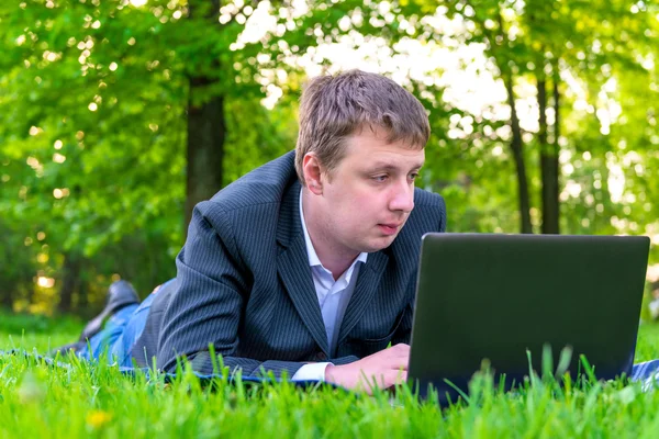 Empresário intensamente trabalhando em um laptop na grama — Fotografia de Stock