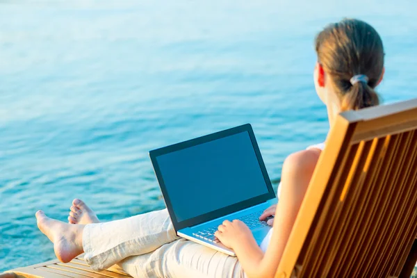 Ragazza a piedi nudi con un computer portatile sulla spiaggia di lavoro — Foto Stock