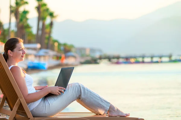 Chica con un ordenador portátil mirando al mar por la mañana — Foto de Stock