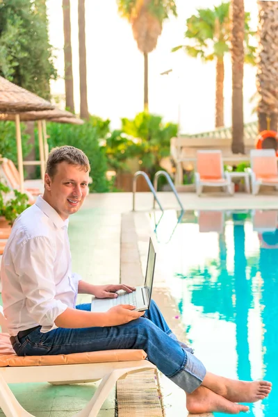 Retrato de hombre con un portátil junto a la piscina en el hotel — Foto de Stock