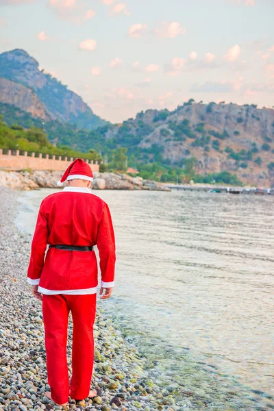 Muž oblečený jako santa claus procházky podél pobřeží — Stock fotografie