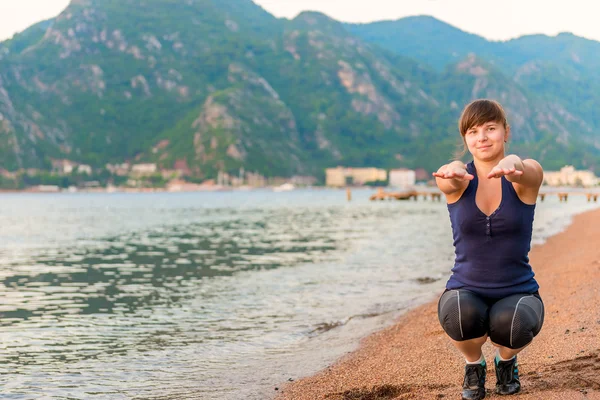 Vacker flicka utför knäböj på sanden nära havet — Stockfoto