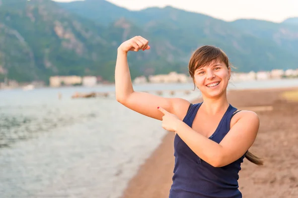 Happy girl showing muscles on the beach — Stock Photo, Image