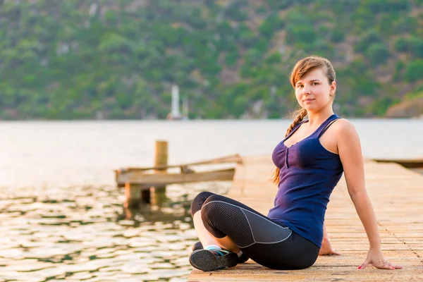 Junge Brünette sitzt auf einem Pier in der Lotus-Position — Stockfoto