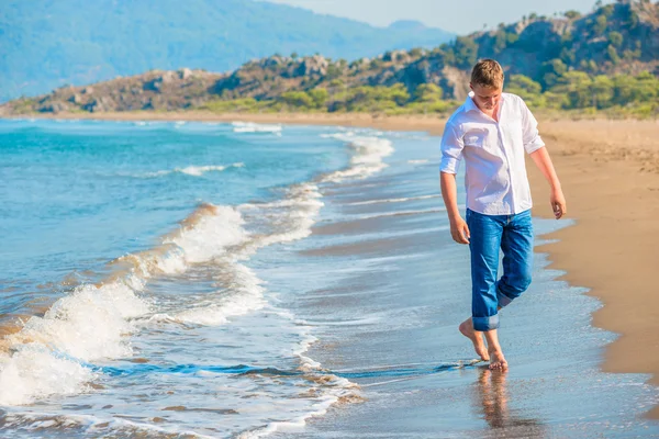 Людина в джинсах і біла сорочка, що йде уздовж узбережжя — стокове фото