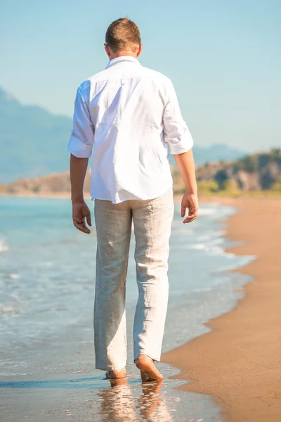 Male in white clothing walking along the beach — Stock Photo, Image