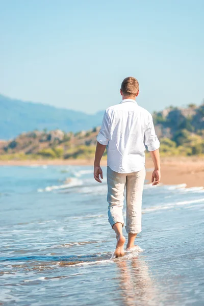 Успешный молодой человек, идущий вдоль песчаного пляжа — стоковое фото