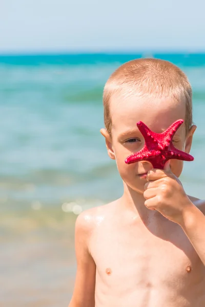 Retrato vertical de um menino com uma estrela vermelha na praia — Fotografia de Stock