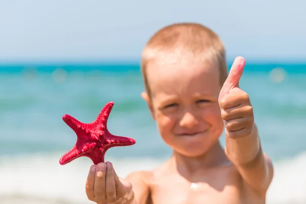 Menino alegre e feliz com estrela do mar na praia — Fotografia de Stock