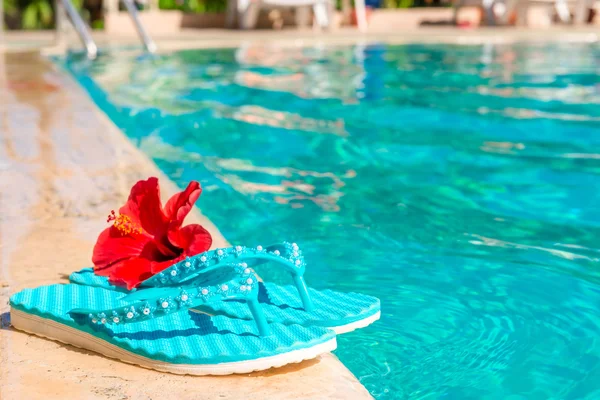 Chanclas de color turquesa y flores en el borde de la piscina — Foto de Stock