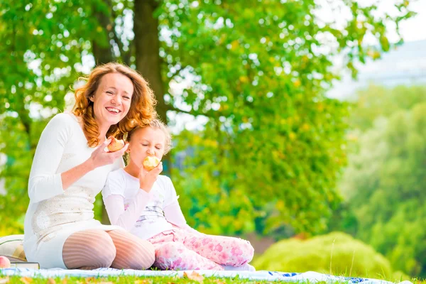 Junge Mutter und ihre Tochter essen Äpfel im Park — Stockfoto