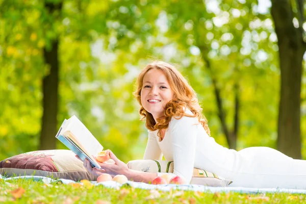 Ragazza ridente con un buon libro sull'erba nel parco estivo — Foto Stock