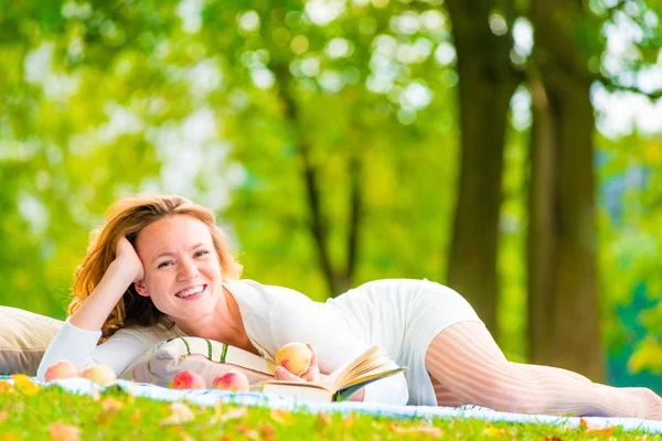 Ragazza dagli occhi marroni con mele e un libro nel parco — Foto Stock