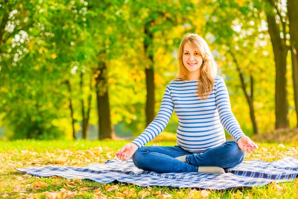 Alegre embarazada en el parque sentado en el loto positio — Foto de Stock