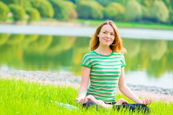 Sonriente chica yogui realiza ejercicios en un parque verde cerca de la la —  Fotos de Stock