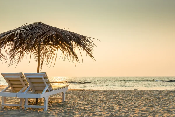 Sedie vuote sotto ombrelloni di paglia su una spiaggia di sabbia — Foto Stock